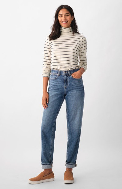 A woman wearing a striped top, blue jeans, and brown shoes stands against a white background. 