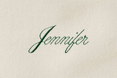 The word "Jennifer" monogrammed in green thread in a thin script font on cream-colored canvas.