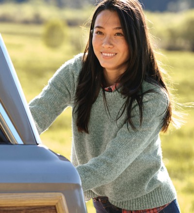 A woman outside wearing a Ragg Wool Sweater, reaching into the back of a car .